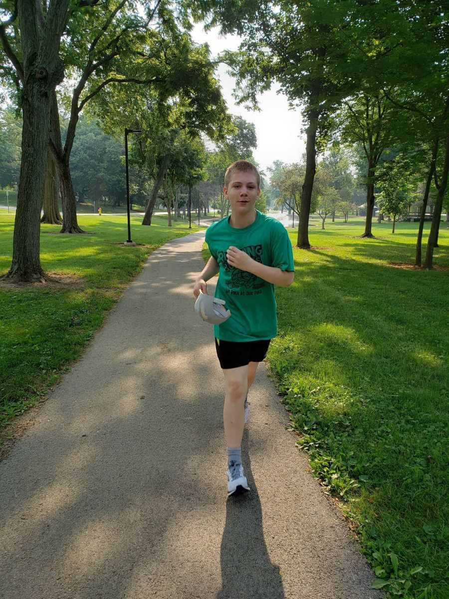 Person running on a paved path in a park, wearing a green shirt and black shorts.