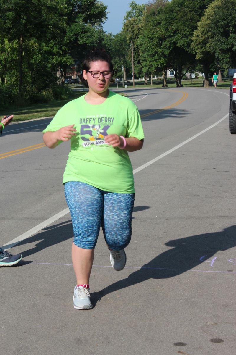 Woman in lime green shirt and blue patterned capris running on paved road.