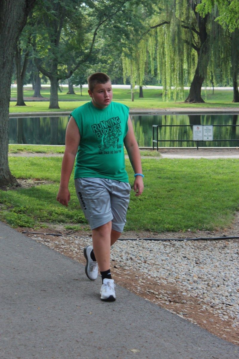 Person in green shirt and shorts walking on a path near a pond.