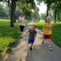 Three people walking on a paved path in a park: a woman and two children.