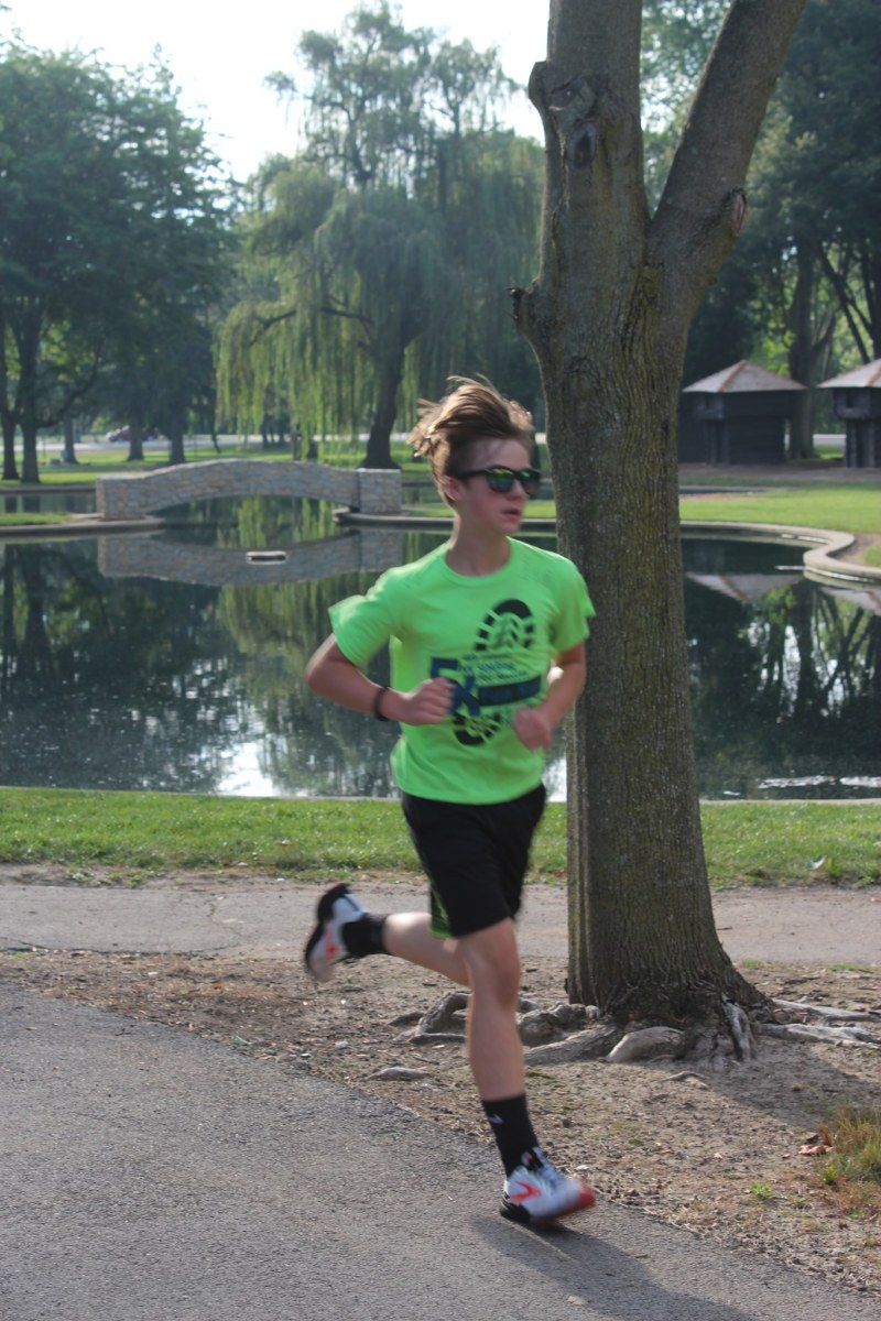 Person running on a path in a park. A pond and trees are in the background.