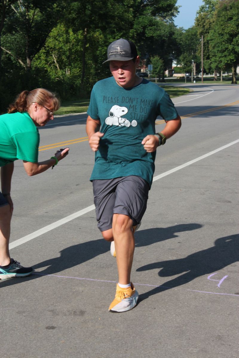 Man running towards the finish line, timer held by woman. Road setting, sunny day.