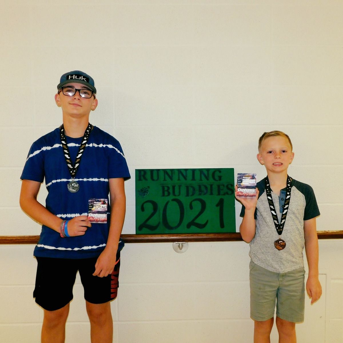 Two boys stand with medals and race info near a 