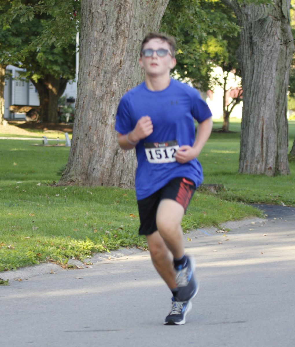Runner in blue shirt and black shorts with race bib #1512 on a paved path.