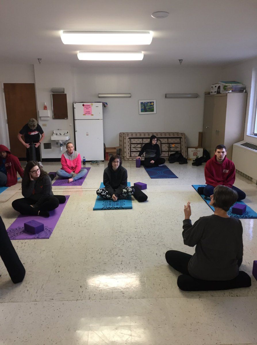 People in a room sit on mats with instructor, practicing yoga.