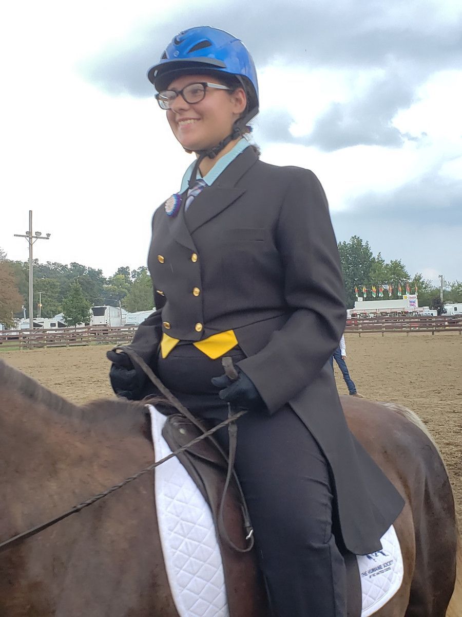 Person riding a horse in an arena wearing a blue helmet and riding jacket, smiling.
