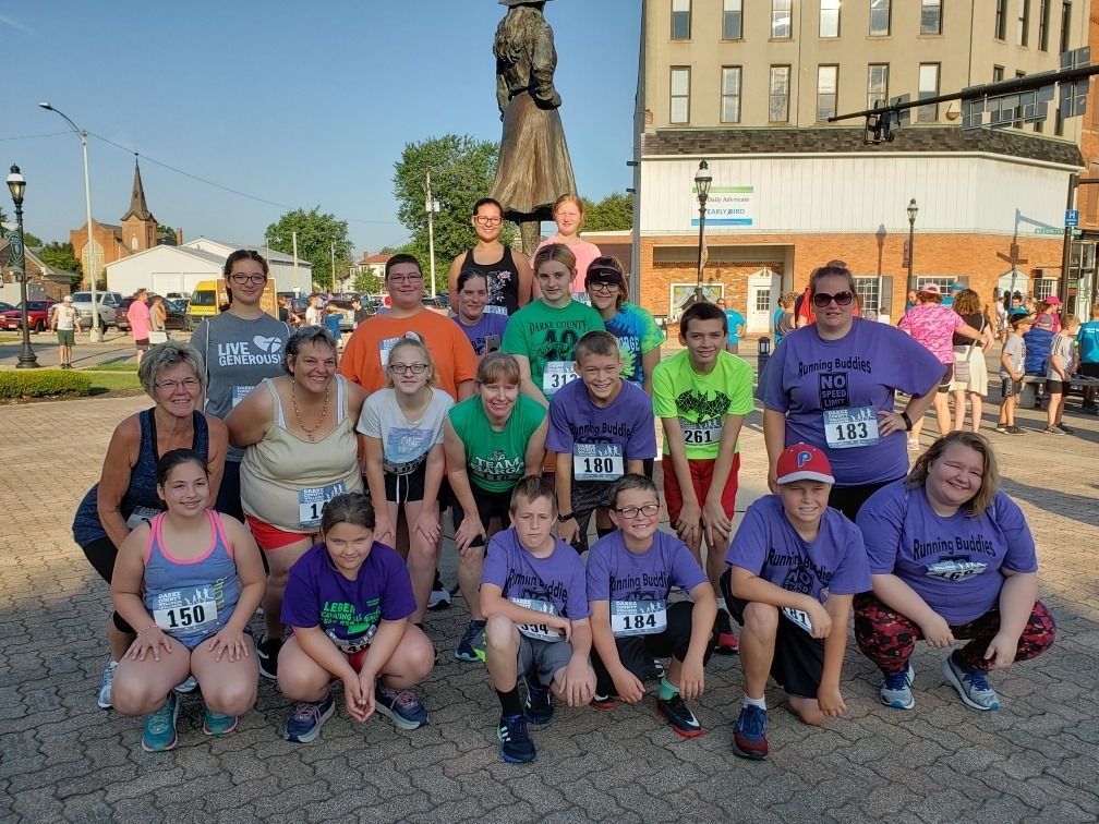 Group of people in running attire, smiling, in front of a statue and buildings.