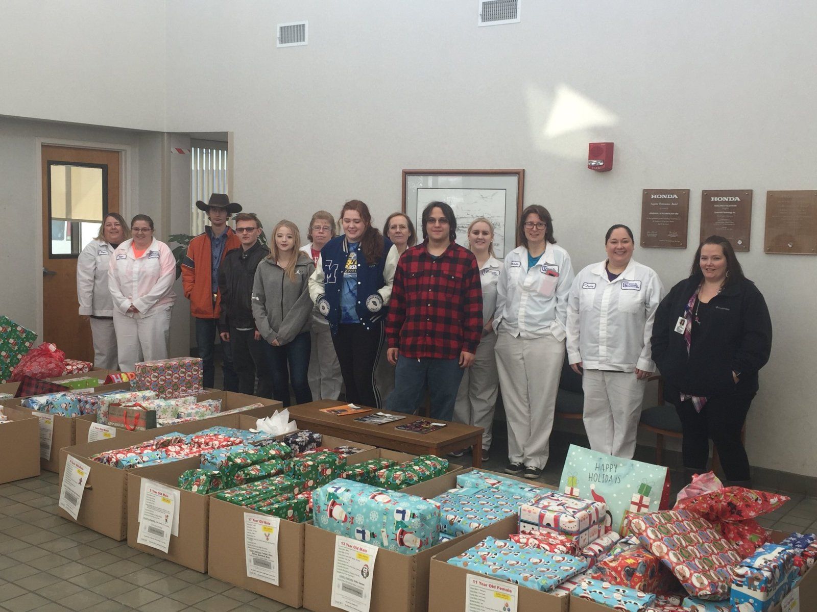 Group of people standing with wrapped gifts in boxes; indoor setting.