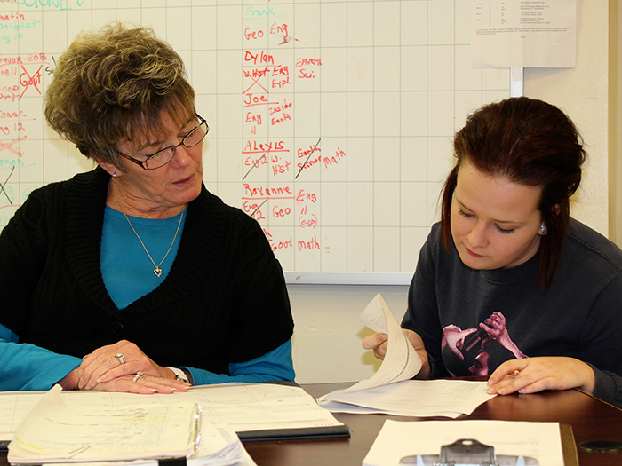 Two women reviewing documents at a table; whiteboard with writing in background.