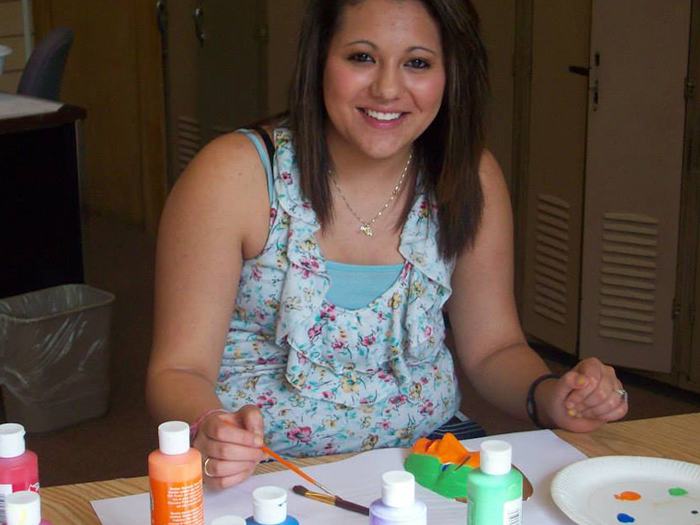 Woman smiling, painting with brushes and paint bottles on a table.