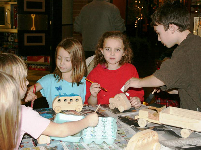 Children painting wooden toy cars at a table, using paint and brushes.