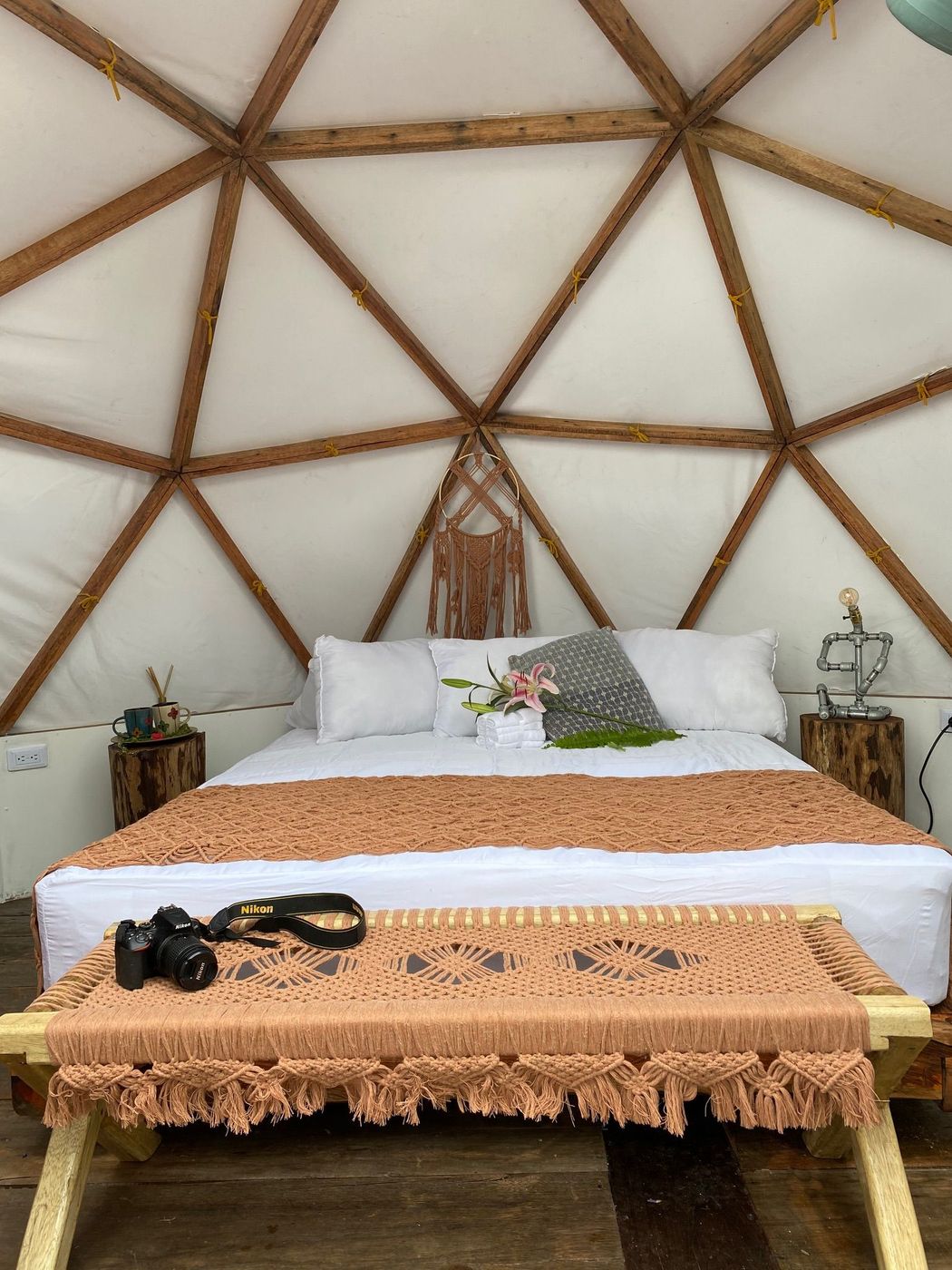 Acogedor dormitorio en una estructura abovedada. Ropa de cama blanca, colcha marrón y vigas de madera.