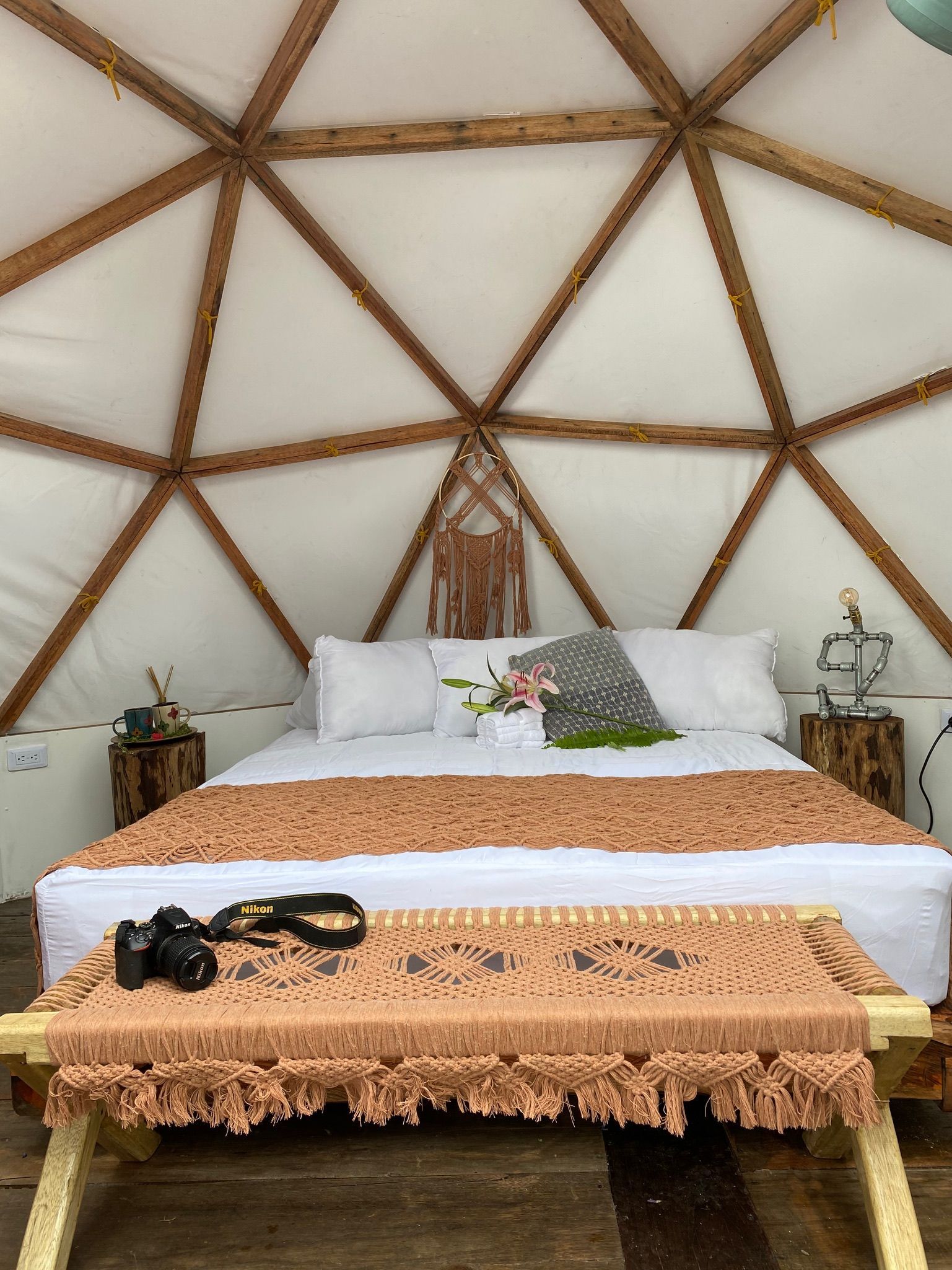 Dormitorio dentro de una cúpula geodésica con cama, mesa pequeña y detalles decorativos.