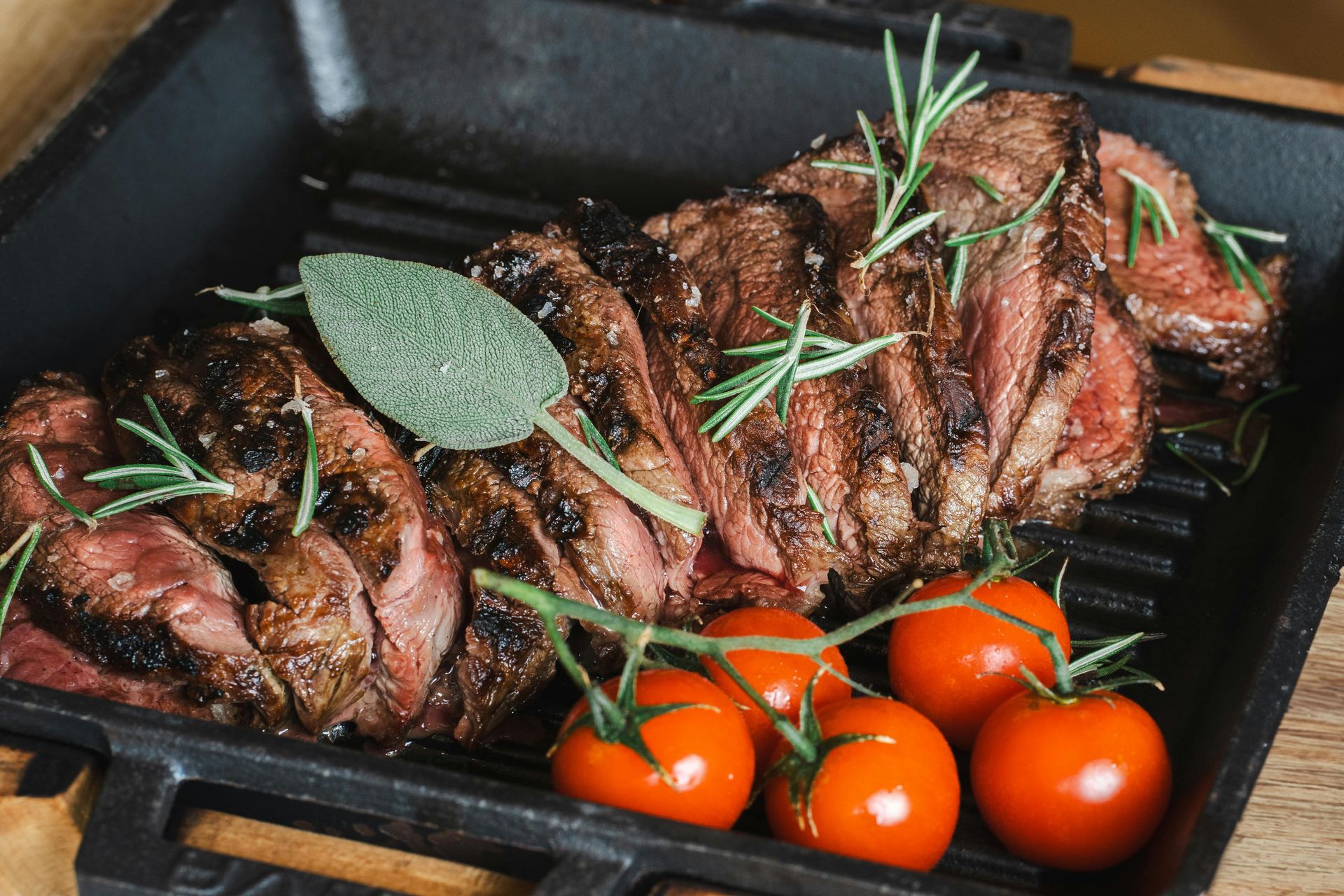 Filete de ternera cortado a la parrilla con romero, salvia y tomates en una parrilla negra.