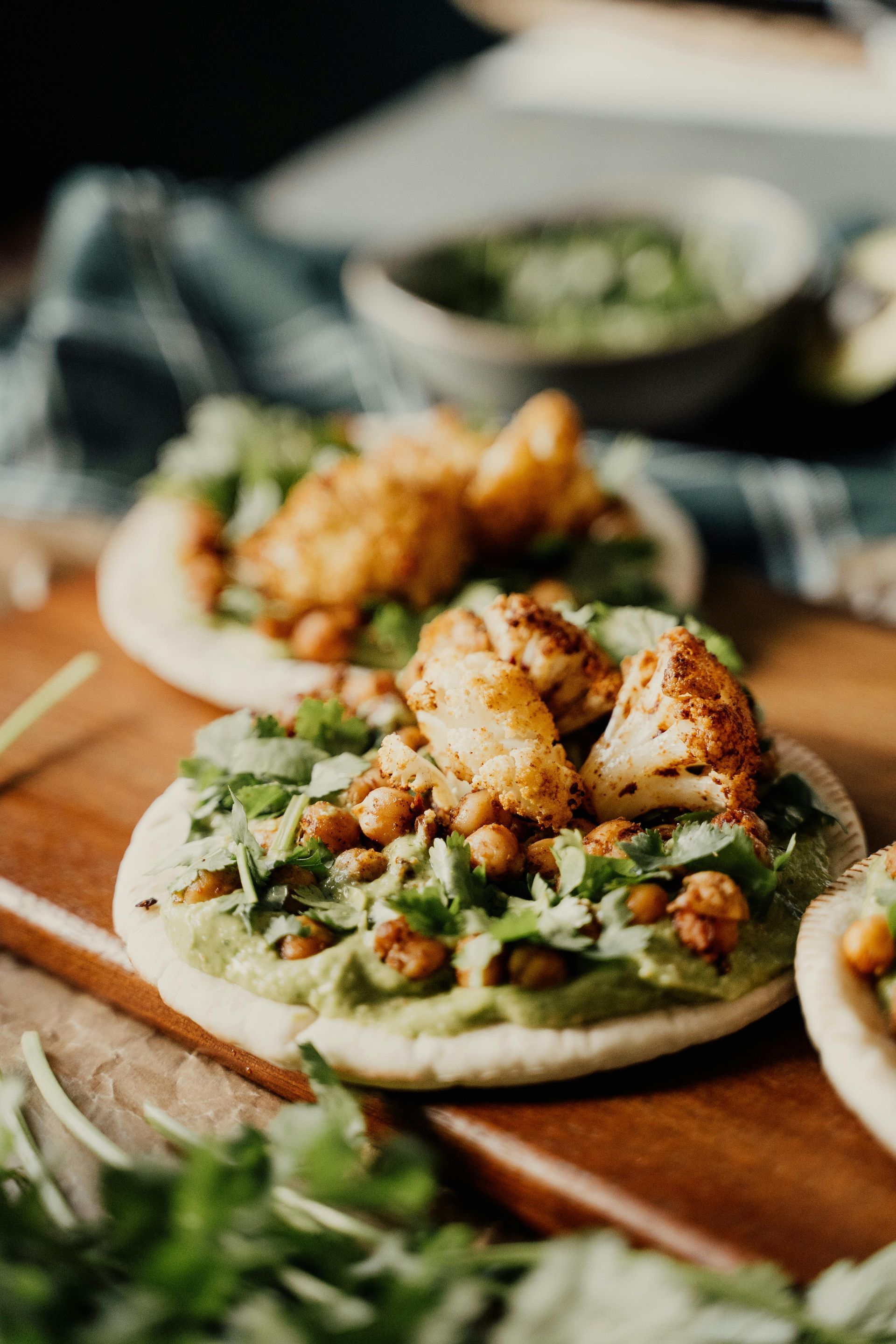 Pan pita cubierto con pasta de aguacate, garbanzos, coliflor asada y cilantro sobre una tabla de madera.