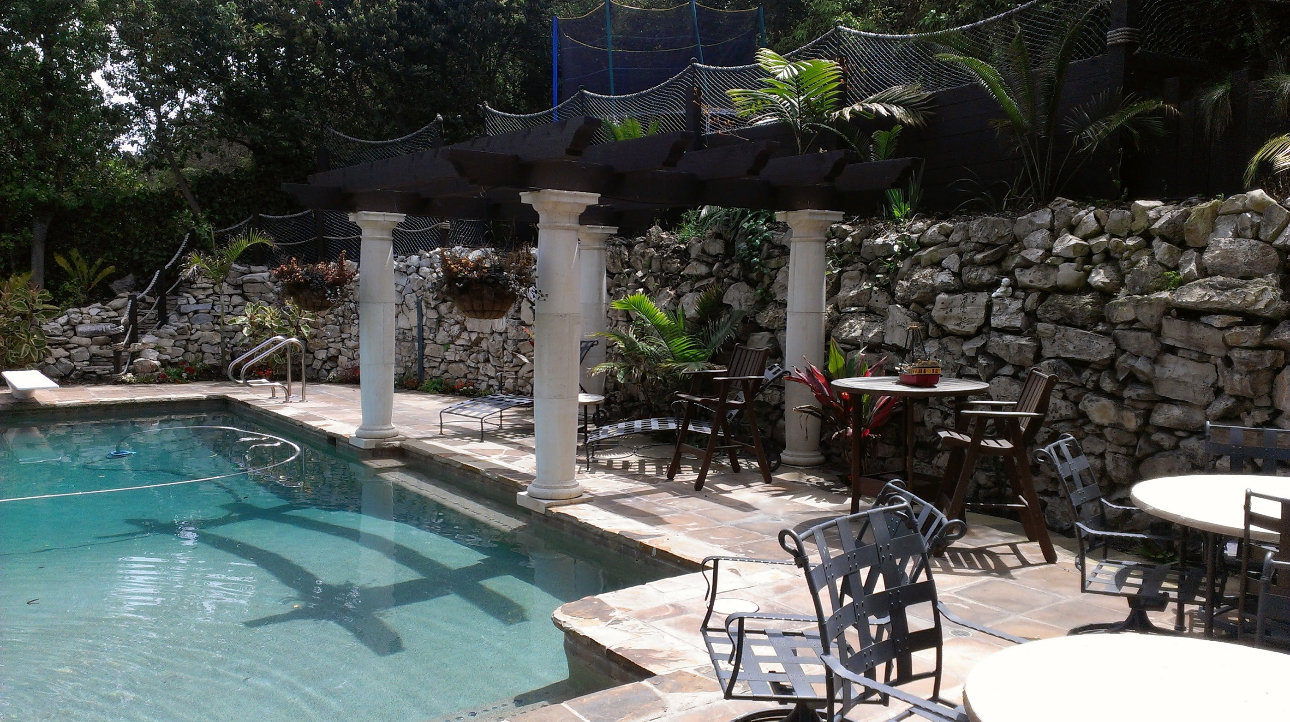 A large swimming pool with tables and chairs around it exhibiting beautiful stonework.