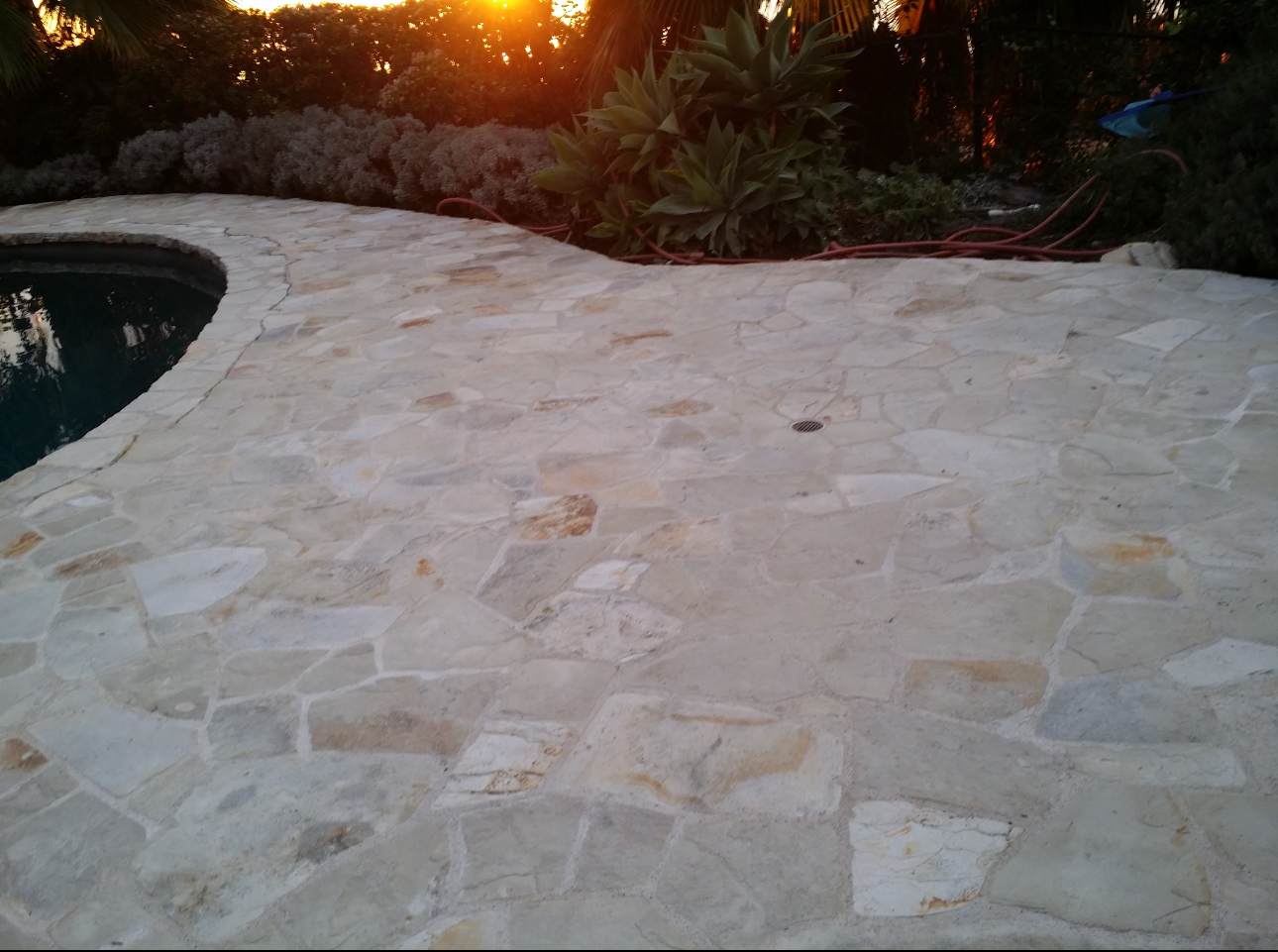 A tiled patio next to a pool with the sun setting in the background