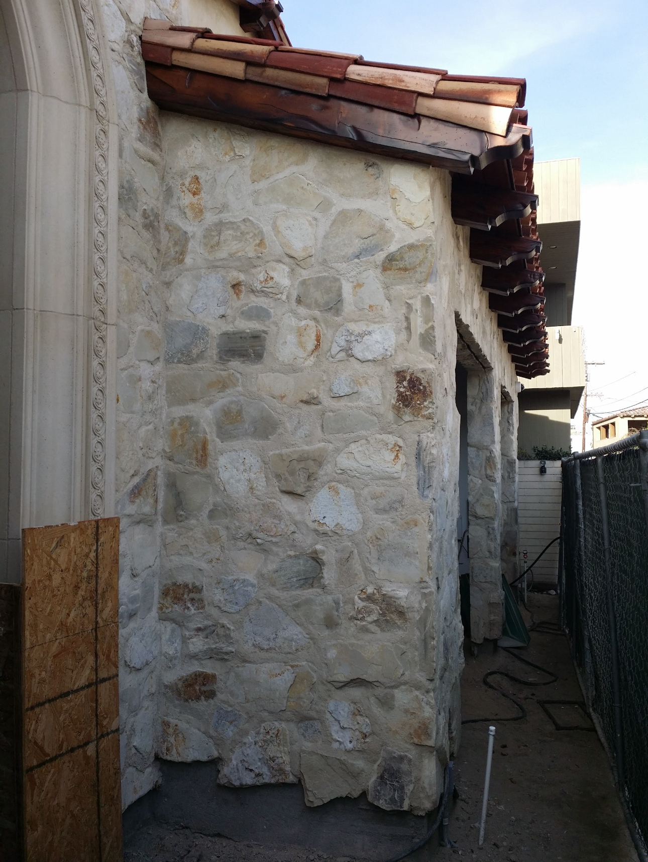 A stone wall with a roof and a fence in the background