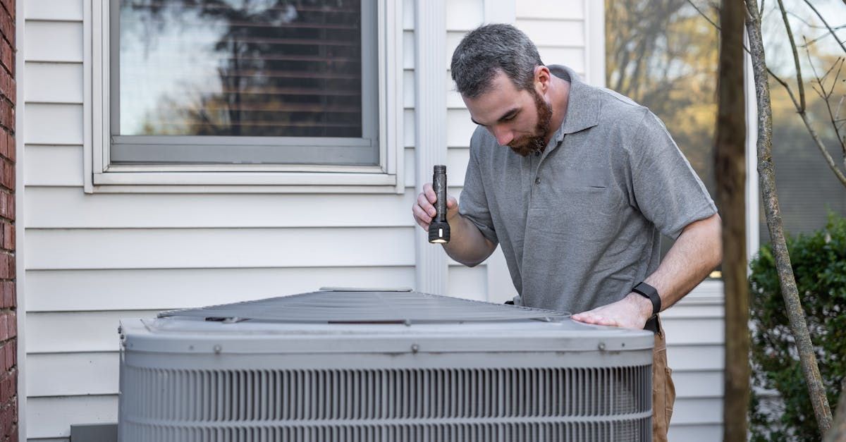 Technician inspecting an outdoor air conditioner unit beside a house