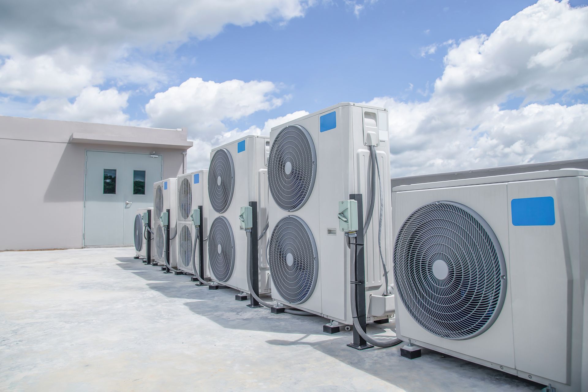 Outdoor row of large white industrial air-conditioning units on a rooftop under a blue sky.