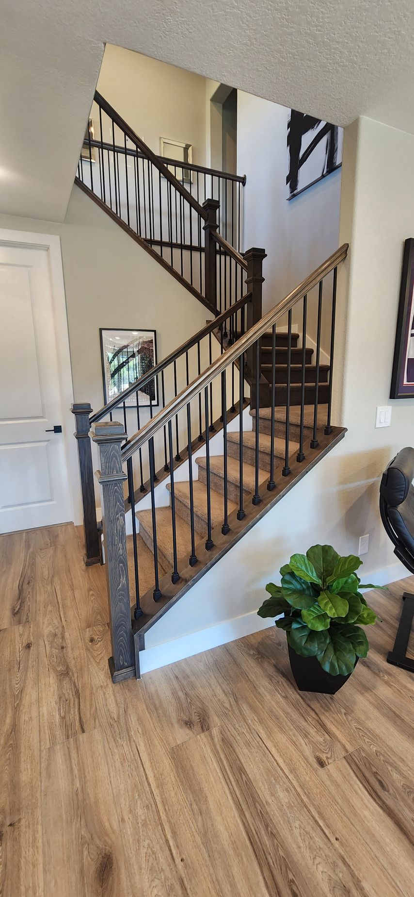 Staircase with dark wood railing and banisters, leading up to the second floor. Wood flooring and potted plant.