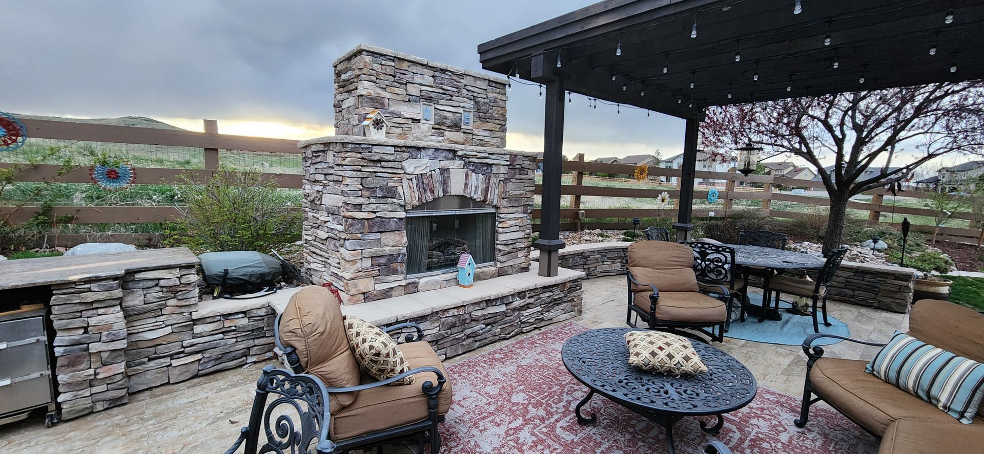 Outdoor patio with stone fireplace, seating area, pergola, and cloudy sky.