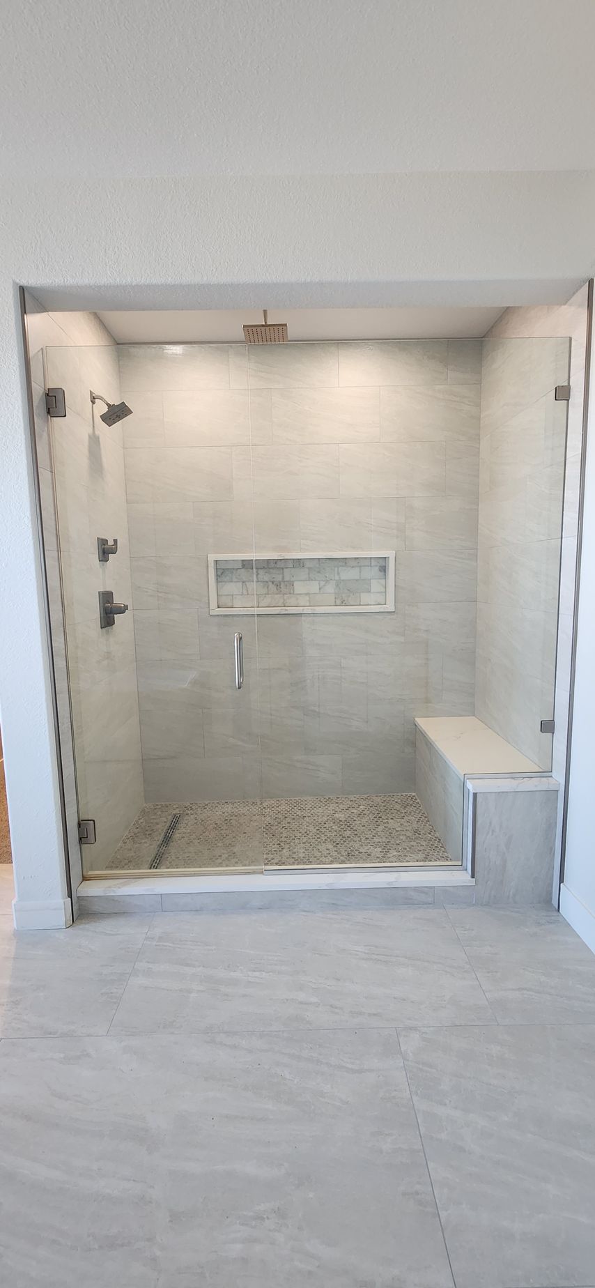 Walk-in shower with pebble floor, built-in bench, and tiled walls.