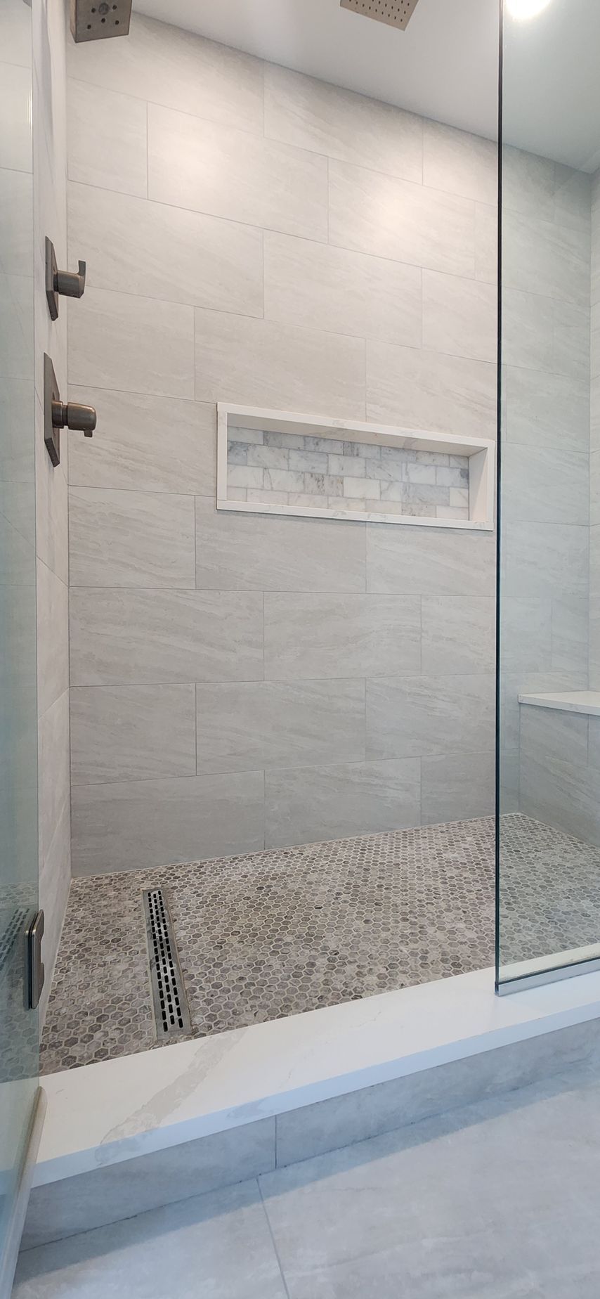 Modern shower with pebble floor, gray tile walls, and glass door.