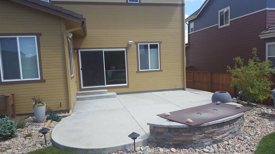 Backyard patio with fire pit, concrete surface, and house in background.