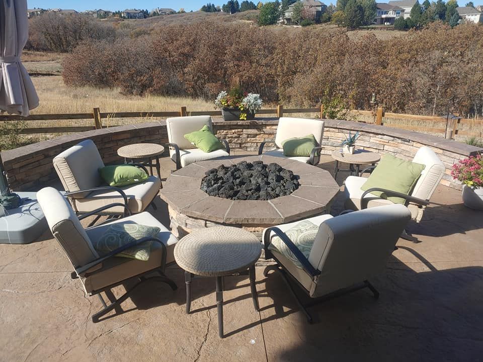 Patio with a stone fire pit surrounded by seating and small tables, against a natural landscape.