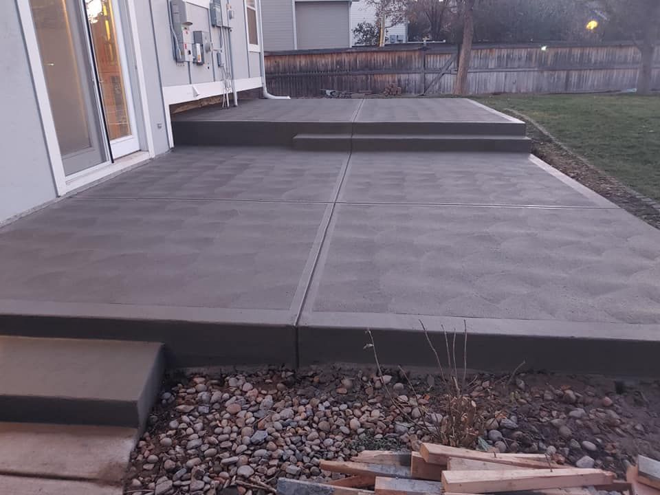 Newly poured concrete patio with steps leading to a raised section, next to a house and yard.