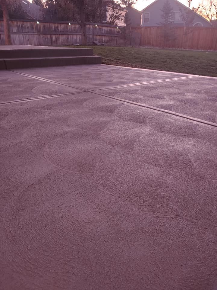 Gray concrete patio with subtle texture, steps, and a backyard fence and lawn.