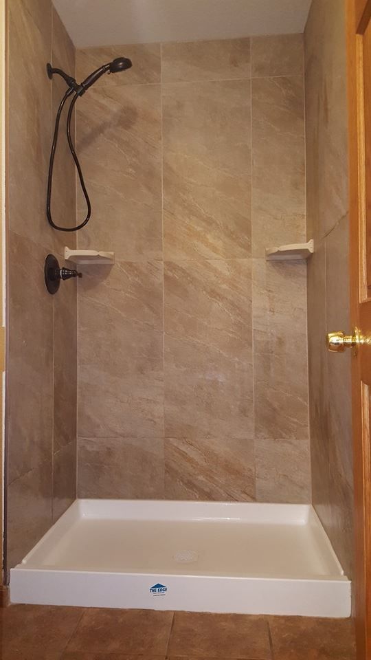 Shower stall with brown tiled walls, white base, and dark shower fixtures.