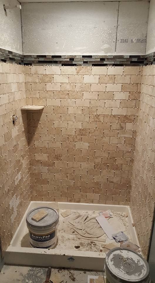 Shower in progress, with beige brick tiles and a shelf. Black and brown mosaic tile border. Gray and white cement.