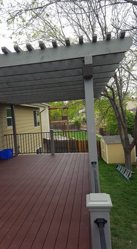Wooden deck with pergola, looking over a backyard. Reddish-brown decking, gray pergola, and green grass.