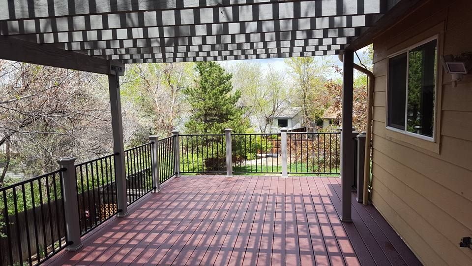 Wooden deck with pergola, black railings, and a view of trees and houses.