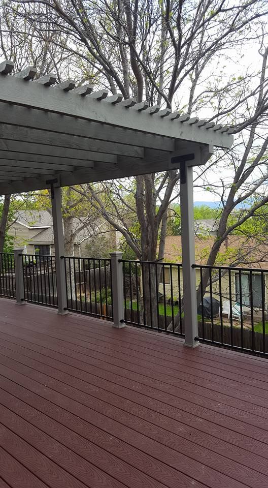 Deck with a pergola, brown decking, black railing, and trees in the background.
