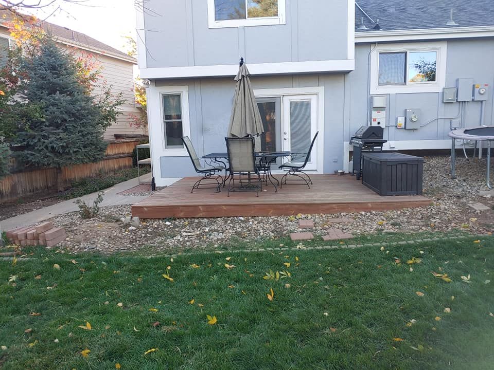 Backyard deck with patio furniture, a grill, and a gray house with a grassy yard.