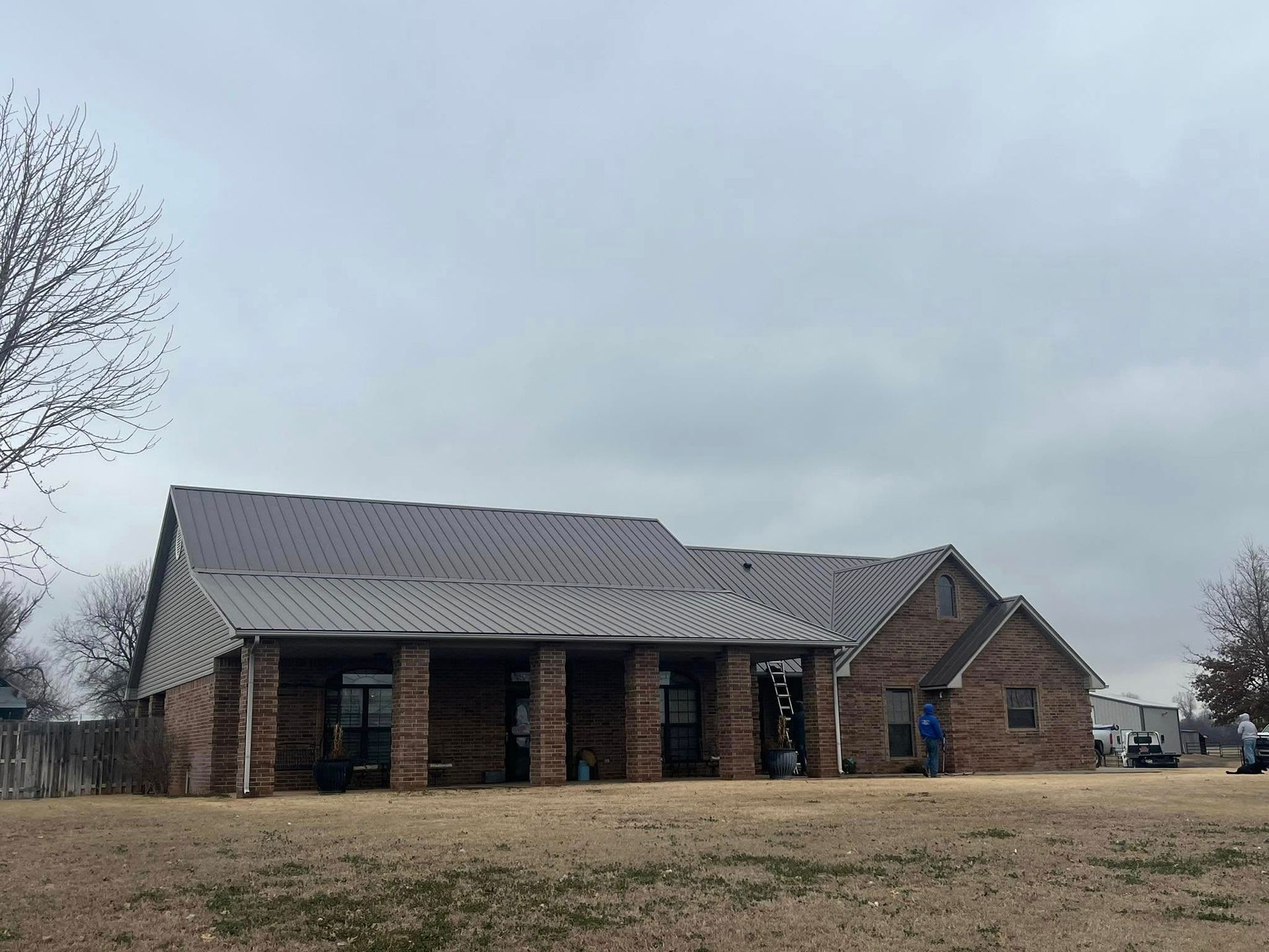 Single-story brick building with a dark metal roof under a cloudy sky.