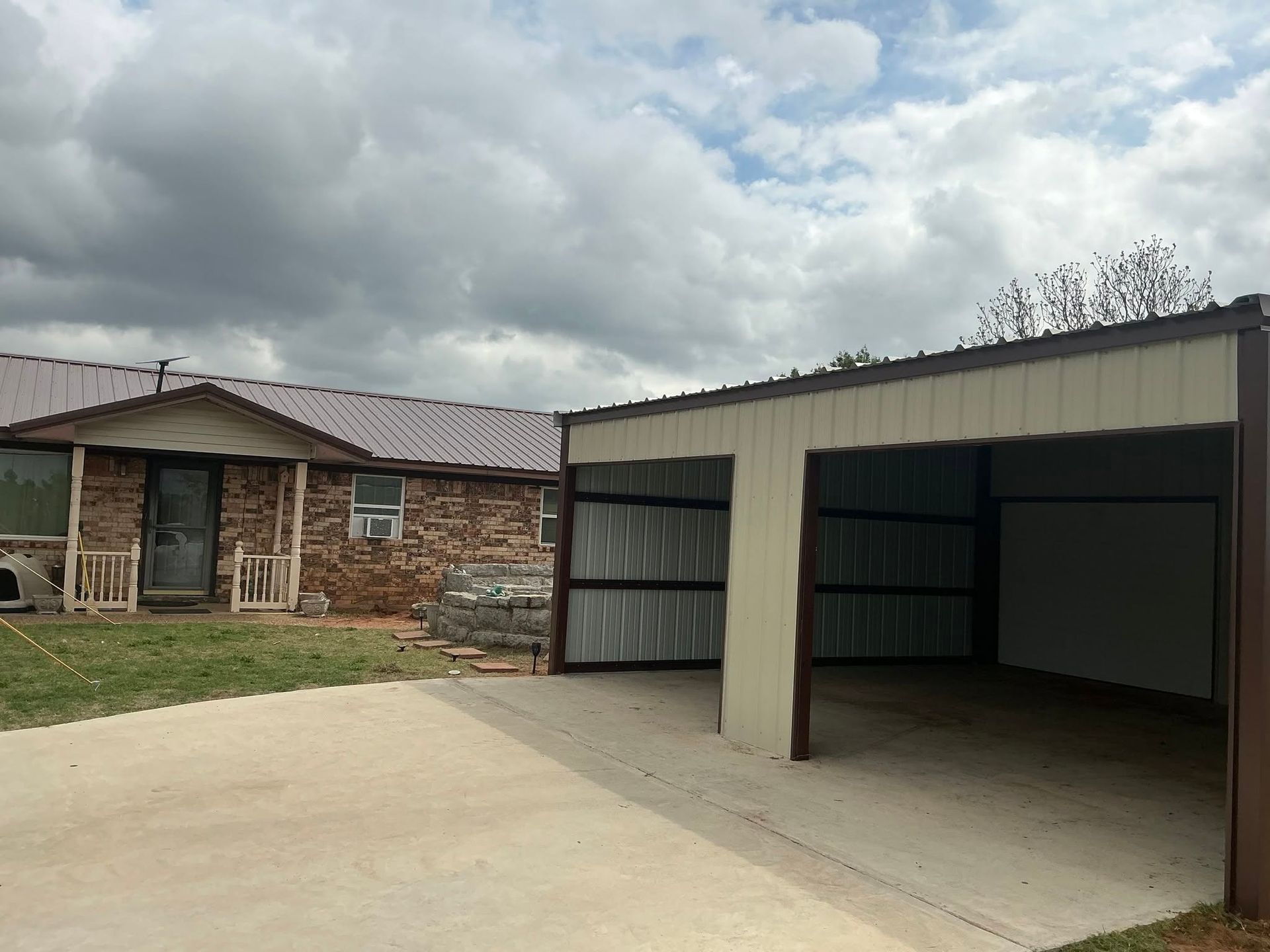 Single-story brick house beside an open metal carport under a cloudy sky
