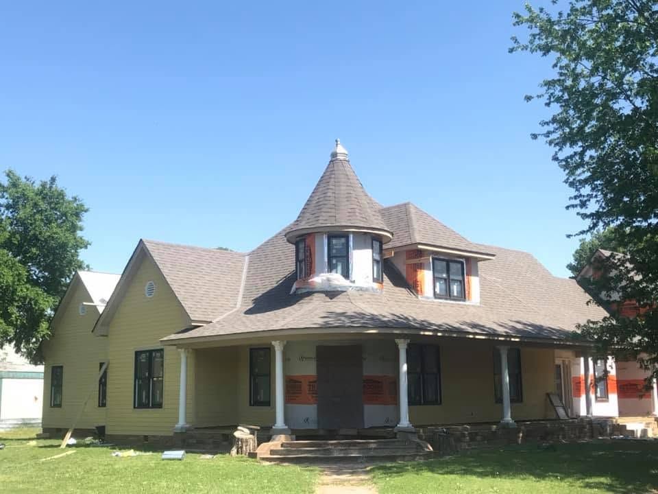 Yellow house with a wraparound porch and turret under a clear blue sky