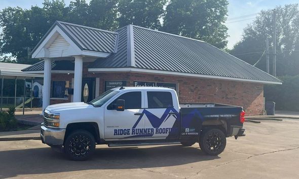 White and blue service pickup truck parked outside a brick building under bright sun