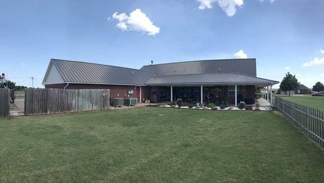 Suburban backyard with a large fenced lawn and a house with a covered patio under a blue sky