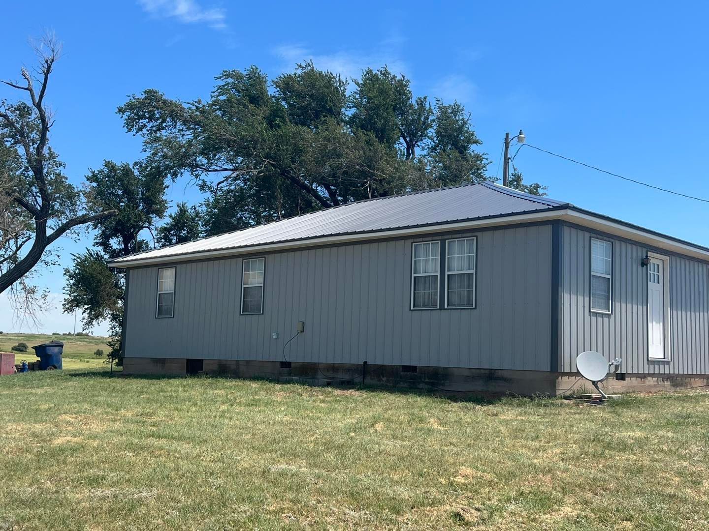 Gray mobile home in a grassy yard under a clear blue sky
