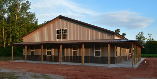 Rustic wooden barn-style building with a metal roof and covered porch on a dirt lot at sunset