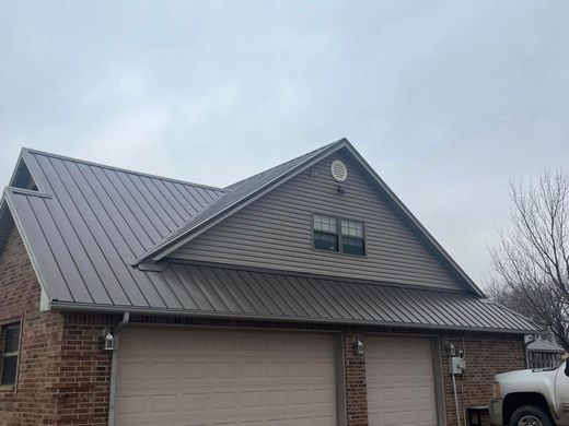 Brick house with dark metal roof and attached garage under an overcast sky
