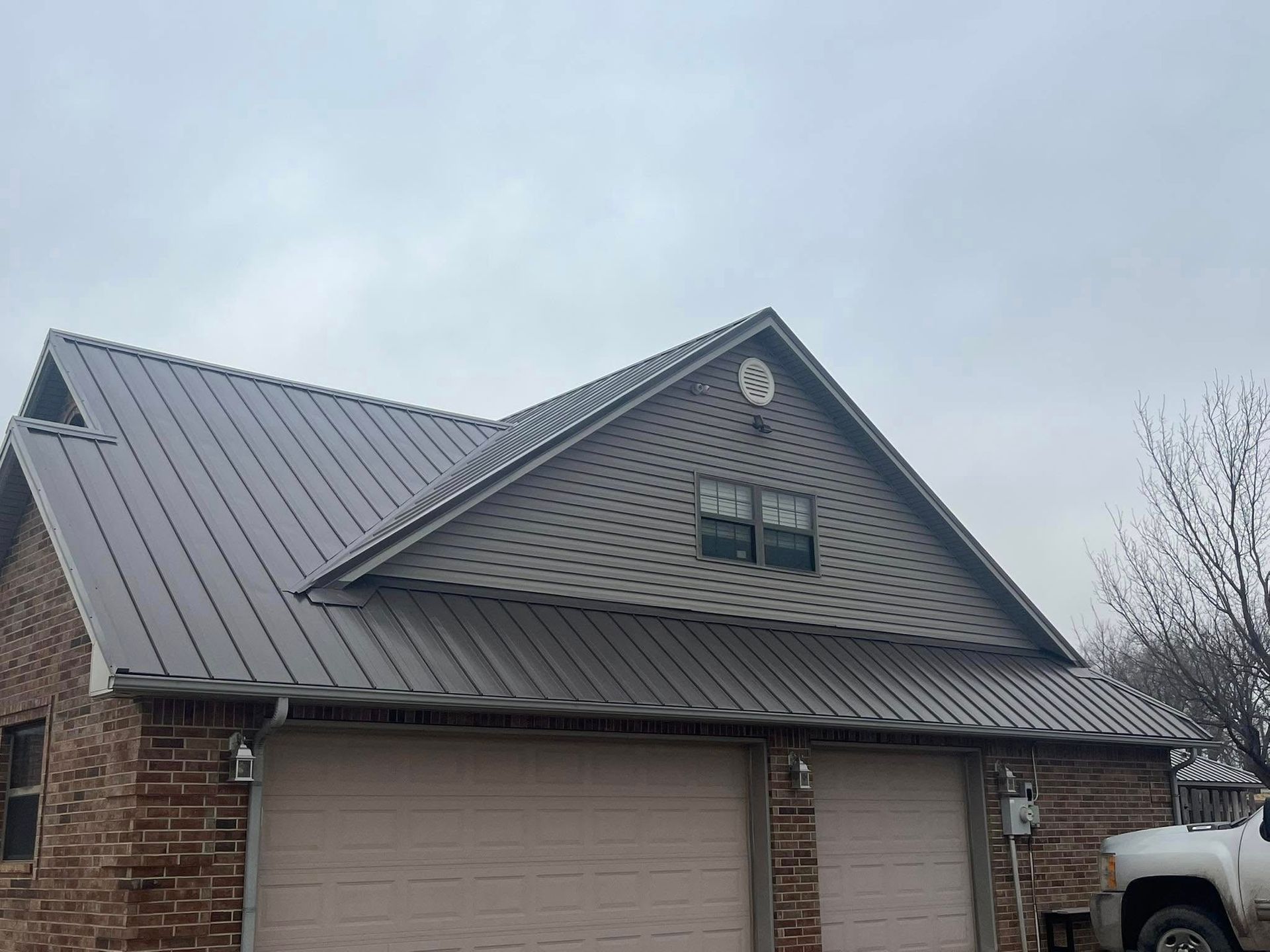 Brick house with a dark metal roof, two-car garage, and overcast sky