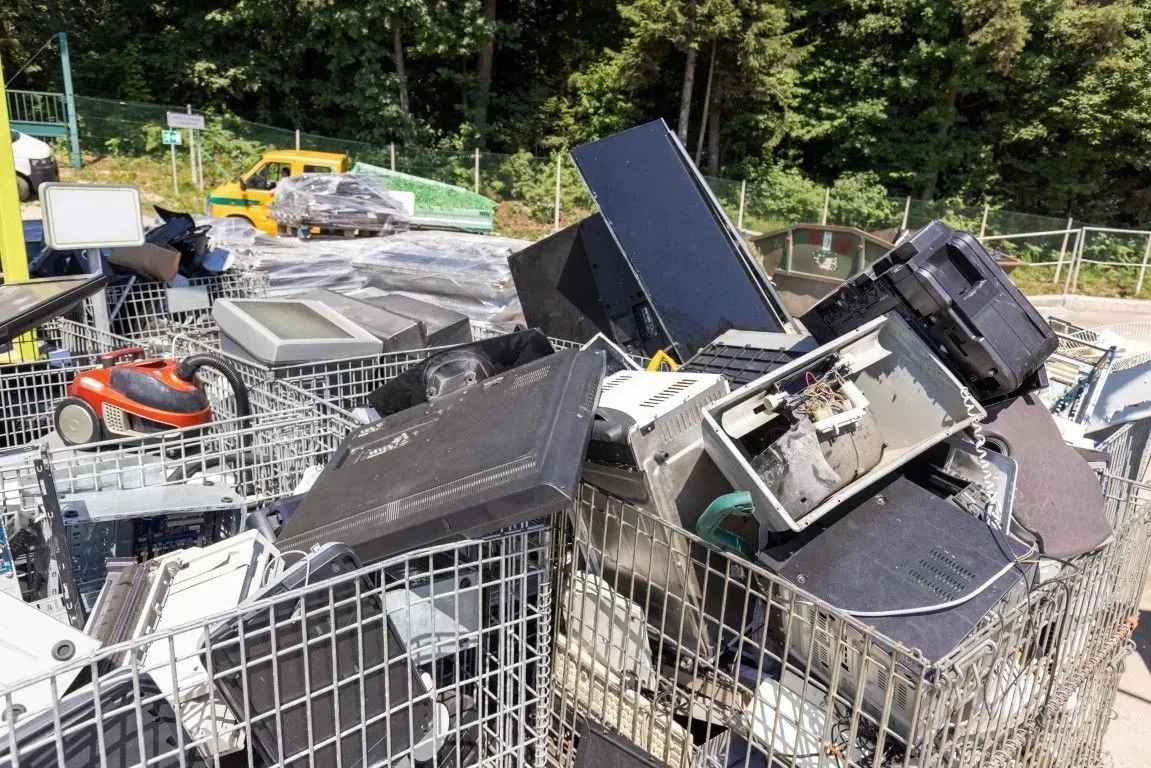 Pile of discarded electronics and appliances in a metal recycling bin.