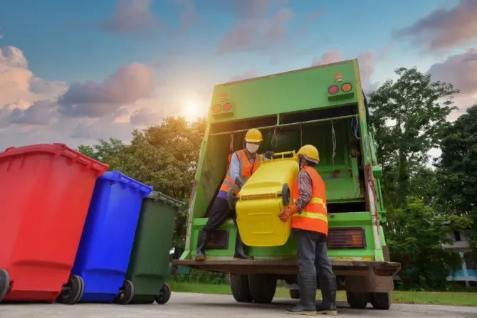 Garbage truck crew loading colorful bins at sunrise on a residential street