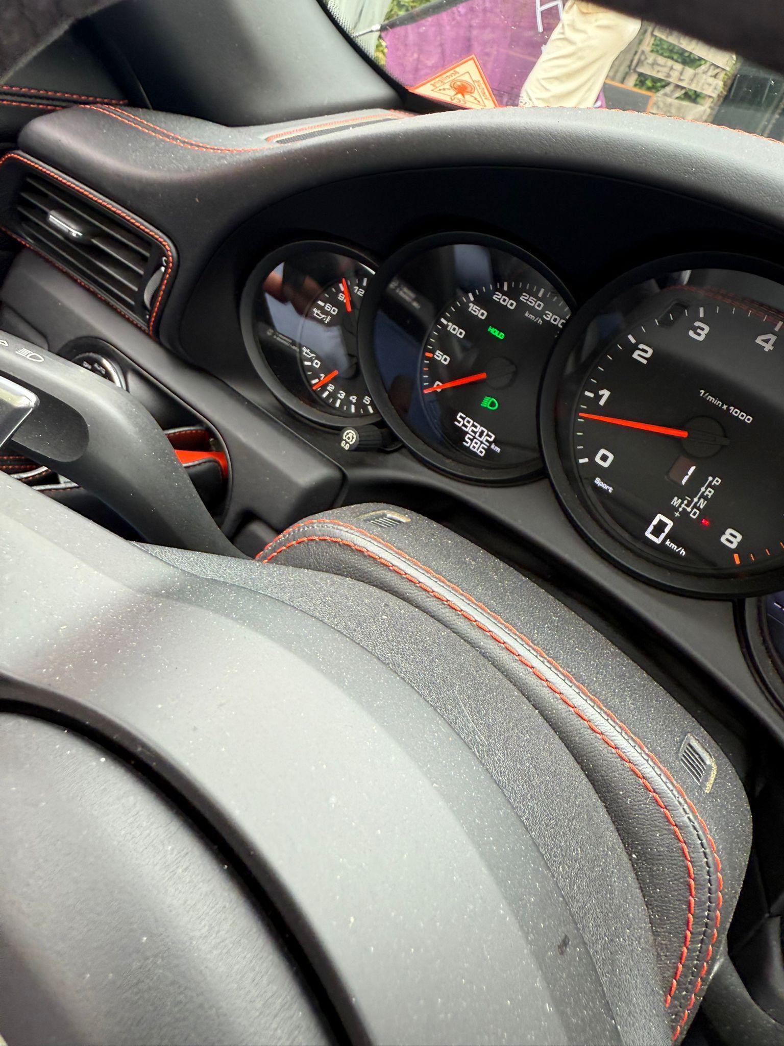 Het dashboard van een auto met meters met wijzers, een stuurwiel en rode stiksels op een zwart interieur.